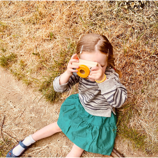 girl of sitting the ground taking a picture with a play camera