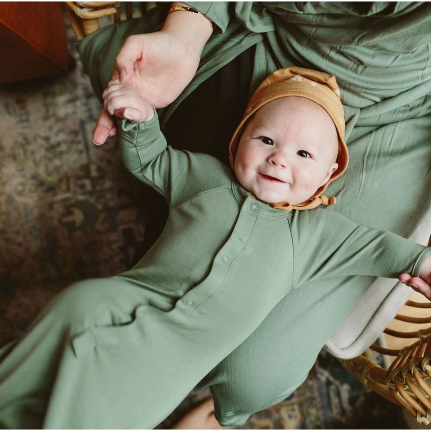 Baby smiling in a gretty onesie and yellow cap