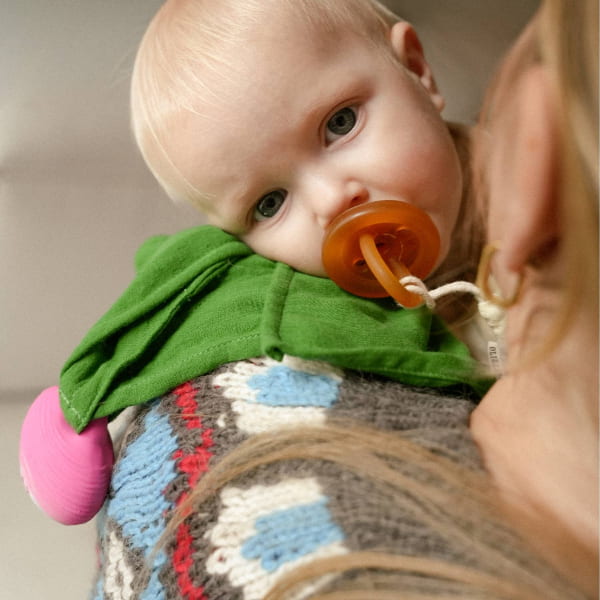 Baby with a pacifier and green bib held by an adult