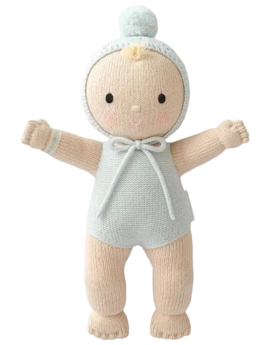 A knitted baby doll with a pale blue bonnet and romper, and beige legs and arms, standing against a plain white background.