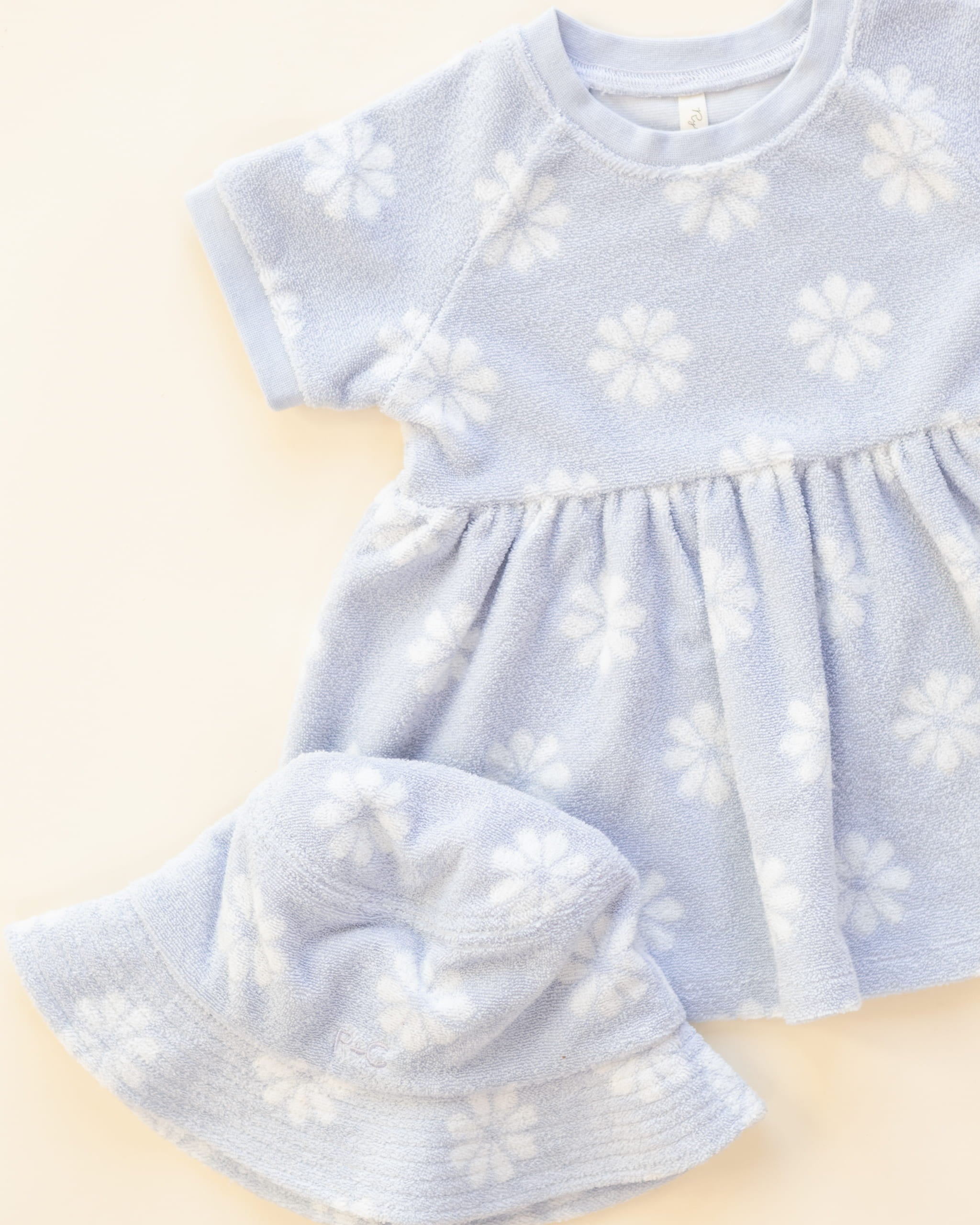 Light blue baby dress with white floral patterns and matching hat on a beige background
