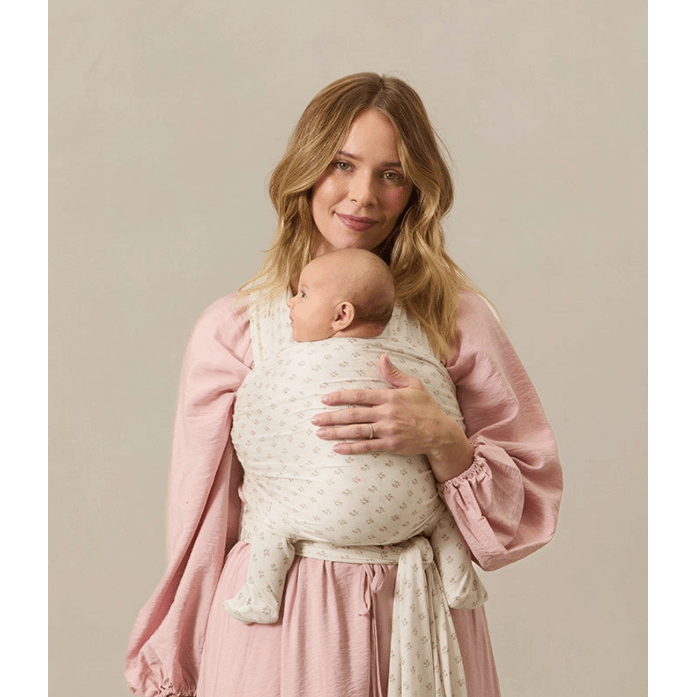 Woman holding a baby wrapped in a sling against a beige background
