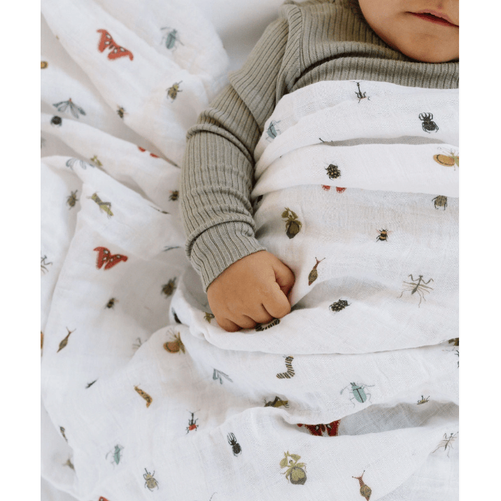 Child wrapped in a white blanket with nature-themed prints, wearing a green sweater.