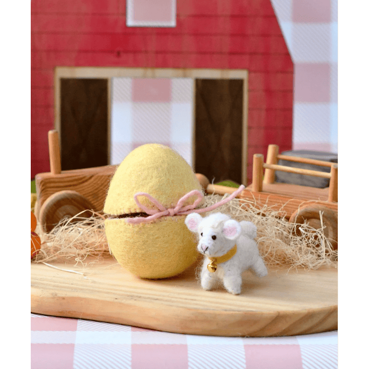 Yellow Easter egg with a small white lamb figurine on a wooden surface with a checkered background.