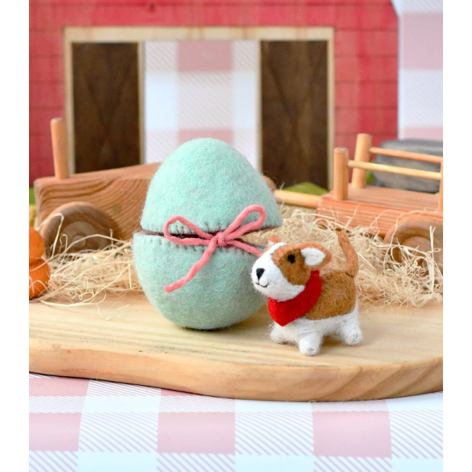 Small dog figurine next to a pastel green Easter egg with a pink bow on a wooden surface.