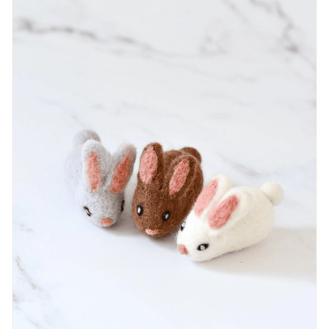 Three felt rabbit toys in gray, brown, and white on a marble surface.