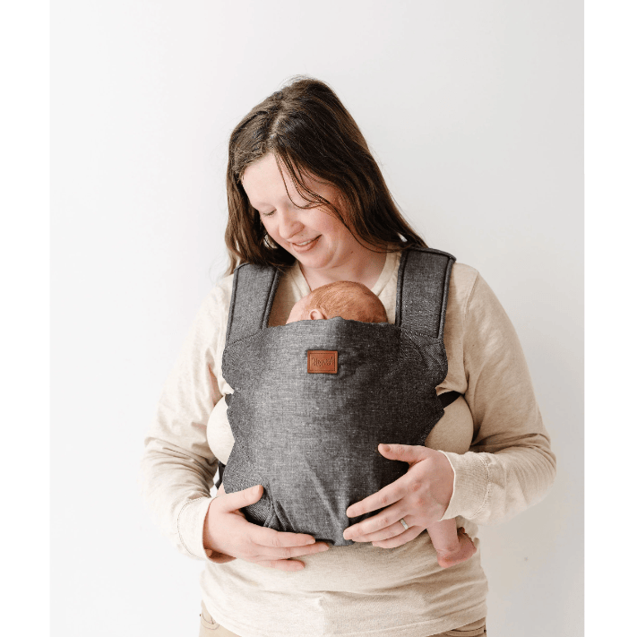 Woman holding a baby in a gray baby carrier against a white background
