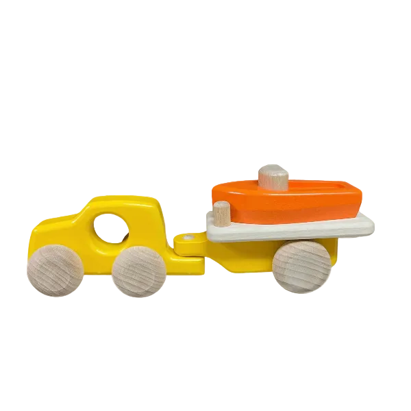 A wooden toy truck with a yellow body and natural wood wheels, pulling a small orange boat on a white trailer, shown against a plain white background.