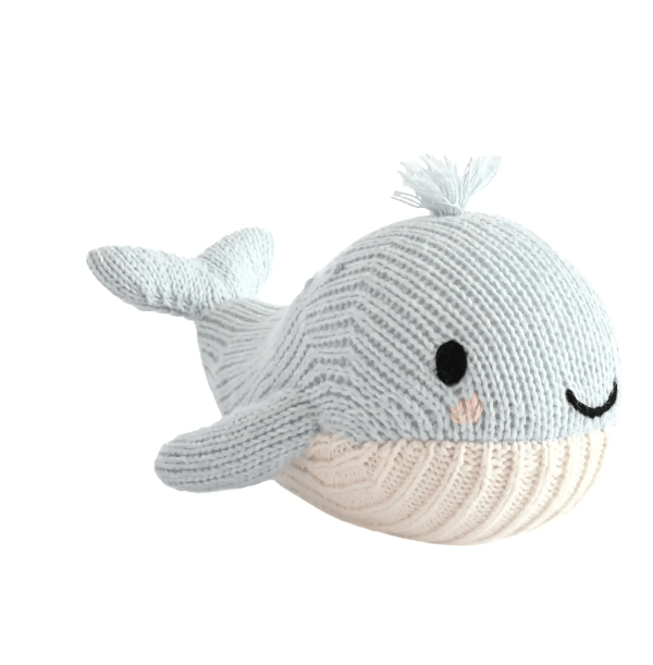 A knitted whale toy with a light blue-gray body, cream-colored underside, black embroidered eyes and smile, and a small tuft of yarn on top, shown on a plain white background.