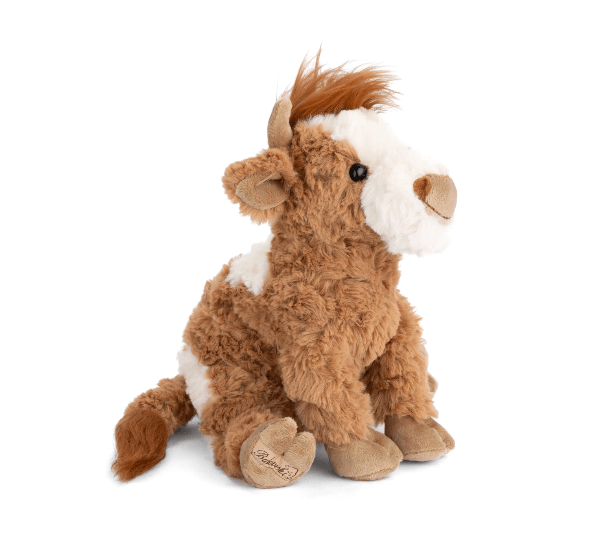 A plush toy cow with brown and white fur, sitting on a clean white background. The toy features curly brown wool-like texture, a white face and belly, small tan hooves, and a small embroidered patch on its foot.