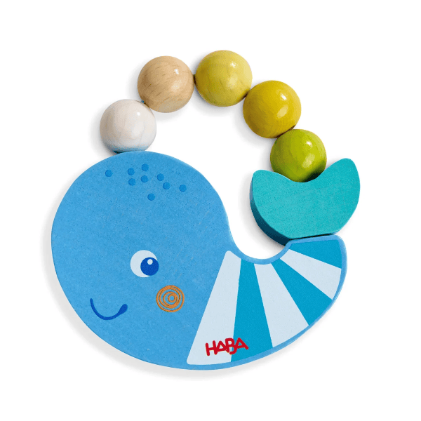 A HABA wooden baby teething toy featuring a blue whale design with a red HABA logo, a turquoise tail, and a beaded loop of natural wood, yellow, and green wooden beads, shown on a white background.