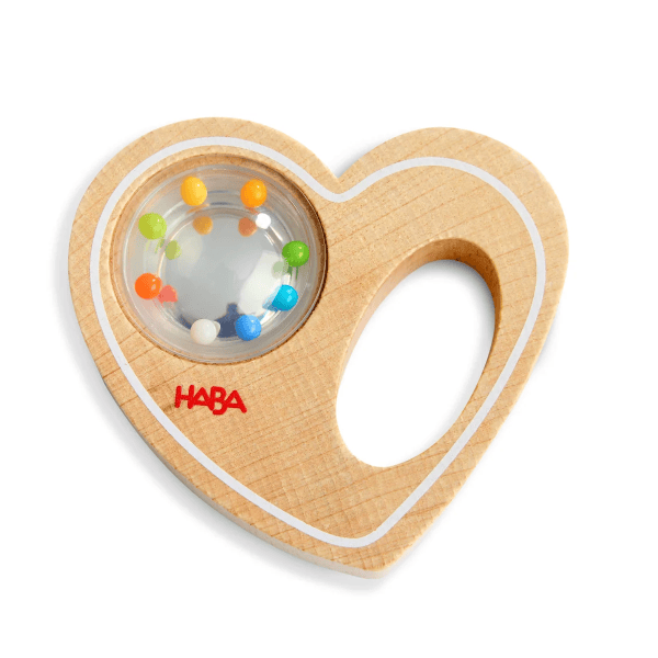 A heart-shaped wooden baby teething toy with a clear circular window containing colorful plastic beads, featuring the red HABA logo on the front, set against a plain white background.
