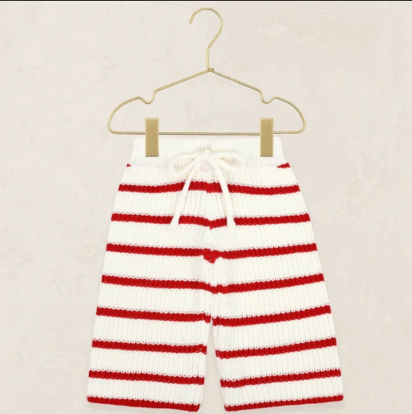 Red and white striped knit pants hanging from a gold wire hanger against a light beige textured background.