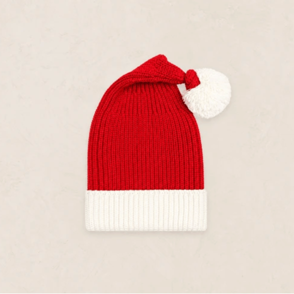 A red and white knit Santa hat with a white pom-pom, displayed flat against a light beige textured background.