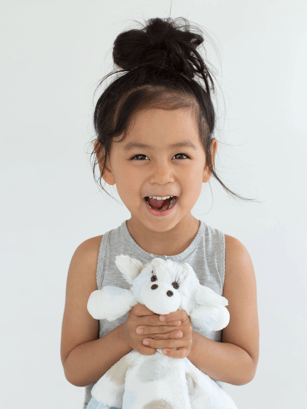 Child holding a white plush toy against a plain background