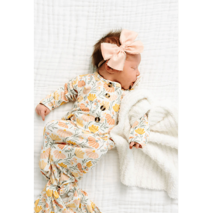 Newborn baby in a floral outfit with a large bow on a white blanket