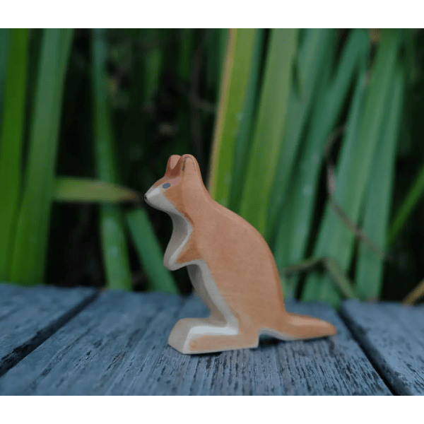 Wooden kangaroo figurine on a wooden surface with green foliage in the background