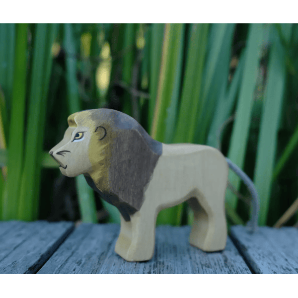 Wooden lion figurine on a wooden surface with green foliage in the background