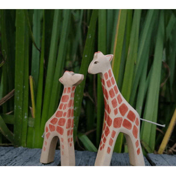 Two wooden giraffe toys standing on a surface with a green leafy background