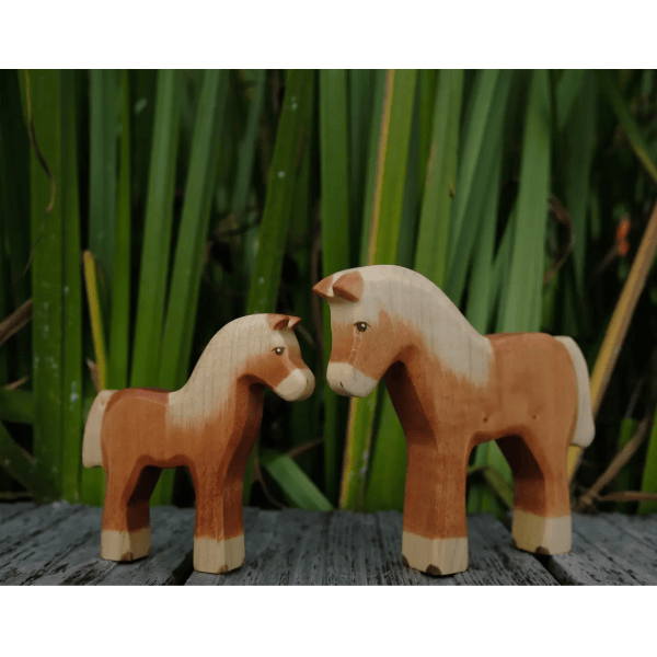 Two wooden horse figurines standing close to each other with a natural background.