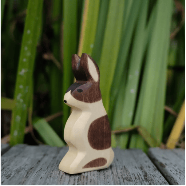 Wooden rabbit figurine with brown and white pattern on a wooden surface with green leaves in the background