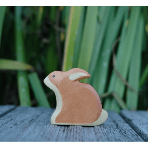 Wooden rabbit figurine on a wooden surface with a green leafy background