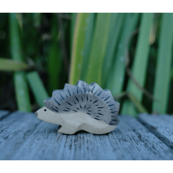Wooden hedgehog figurine on a wooden surface with greenery in the background