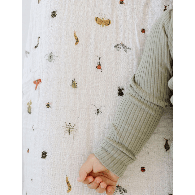 Close-up of a textured fabric with insect patterns and a person's sleeve.