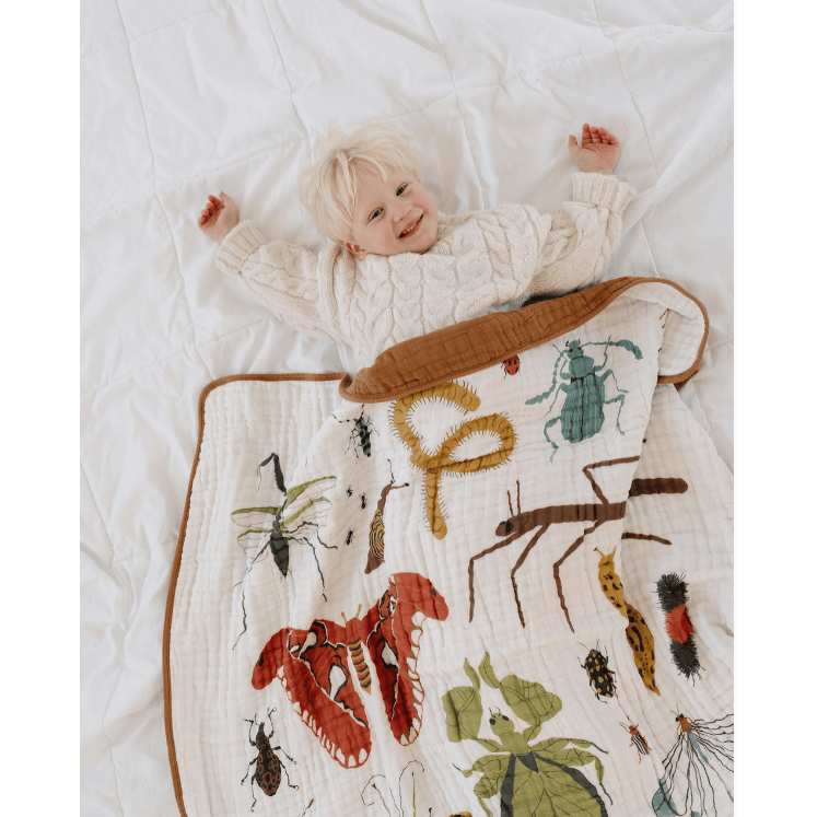 Child lying on a quilt with insect illustrations on a white bed.