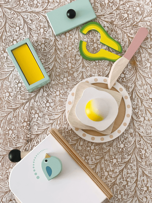 Children's play kitchen set with toy oven, knife, and food items on a patterned surface