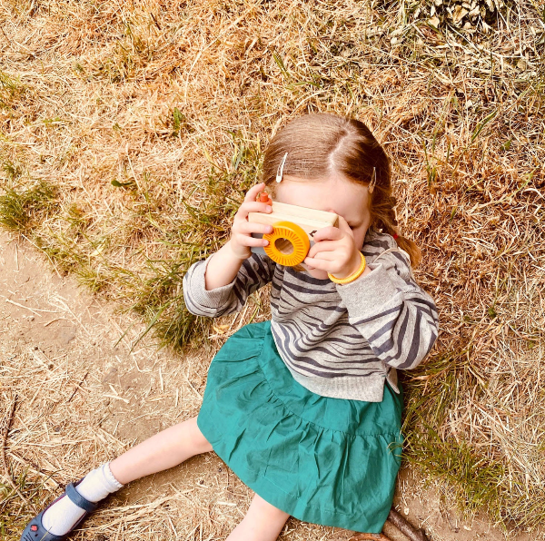 Child playing with a toy camera outdoors on dry grass