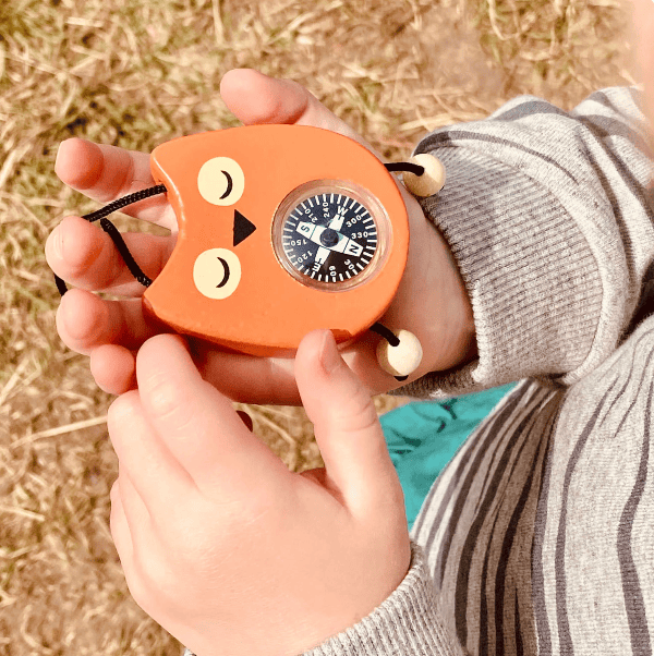 Person holding a compass shaped like a cat face in an outdoor setting