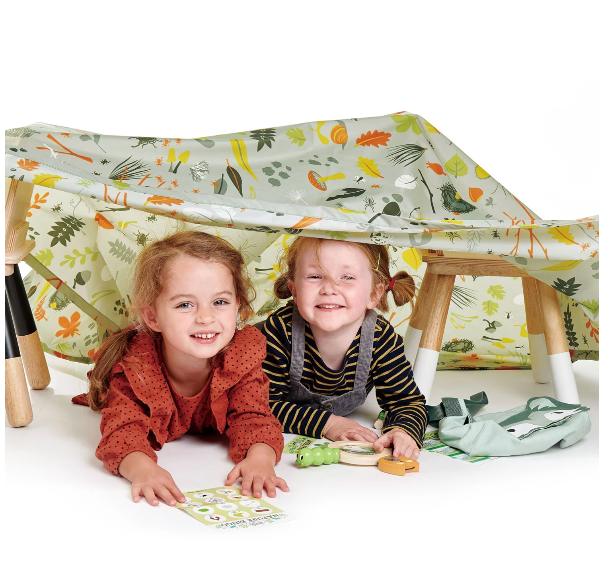 Two children playing under a table tent with a nature-themed design.