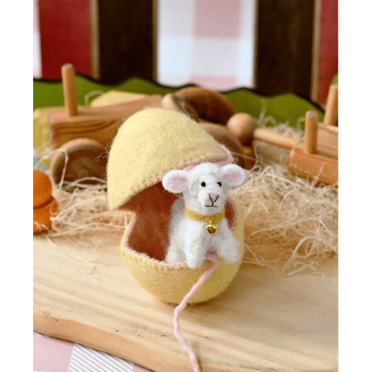 Small white lamb toy with a yellow egg-shaped house on a wooden surface.