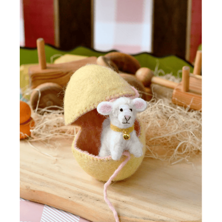 Small white lamb toy with a yellow egg-shaped house on a wooden surface.