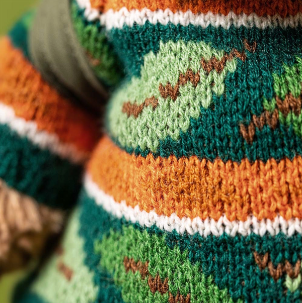 Close-up of a knitted sweater with a pattern of green, orange, and white stripes.