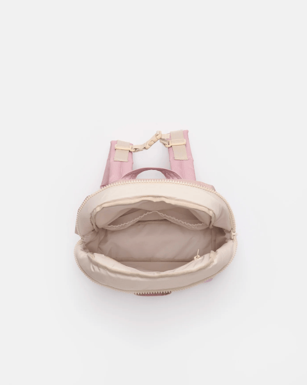 A top-down view of a small pink and beige backpack with the main compartment open, showing the interior lining and a gold-tone chain detail on the strap, set against a plain light gray background.