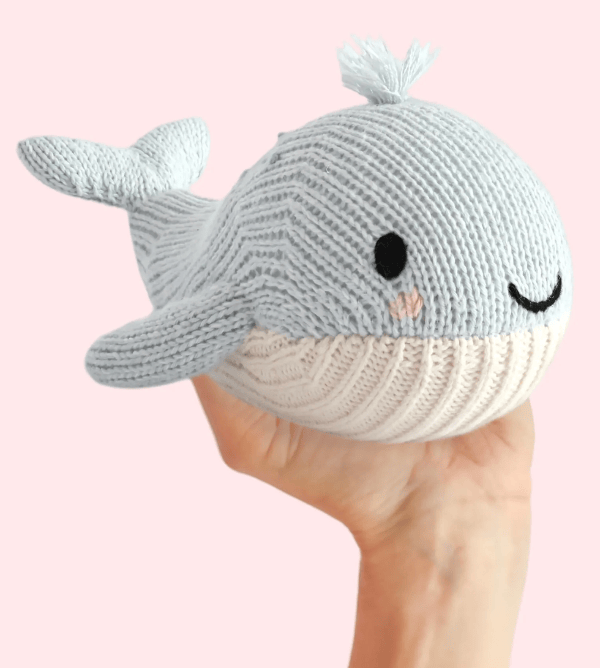 A light blue and cream knitted whale plush toy being held in a person&