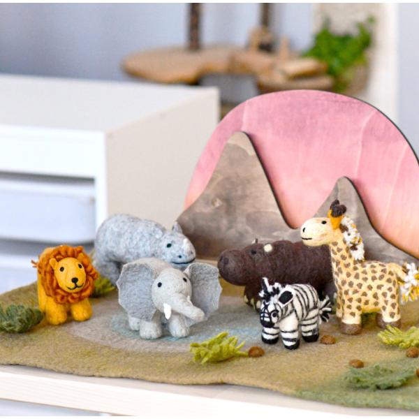 A set of felt animal toys arranged on a textured safari-themed base with a pink and gray mountain backdrop. The animals include a yellow lion, gray hippo, gray elephant, brown rhino, black-and-white zebra, and tan giraffe.