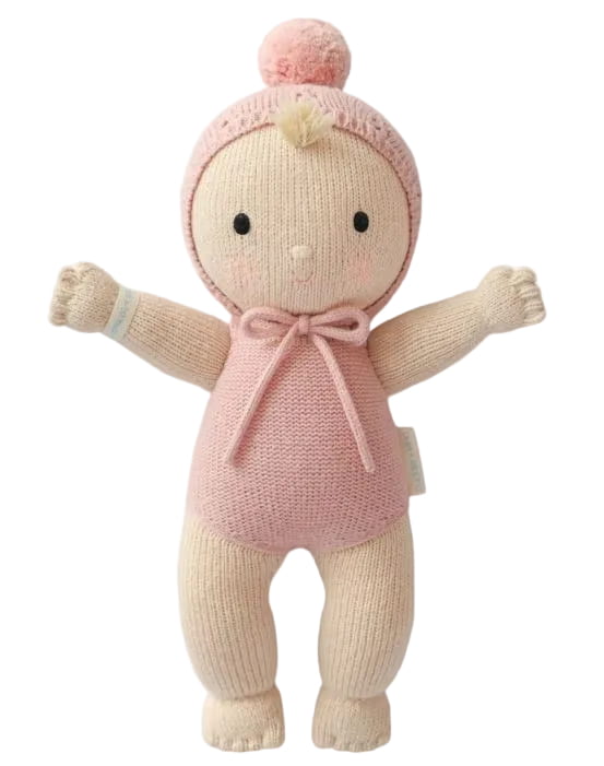 A knitted baby doll with a cream-colored body, pink hat and bodysuit, and black embroidered eyes, shown against a plain white background.
