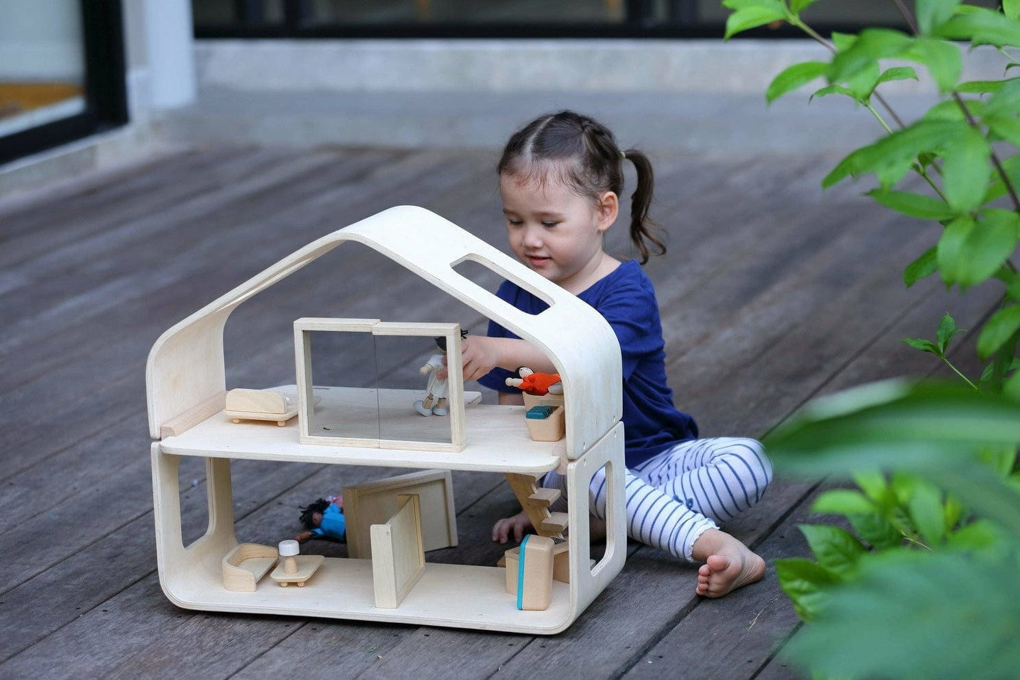 Child playing with a wooden dollhouse on a wooden deck