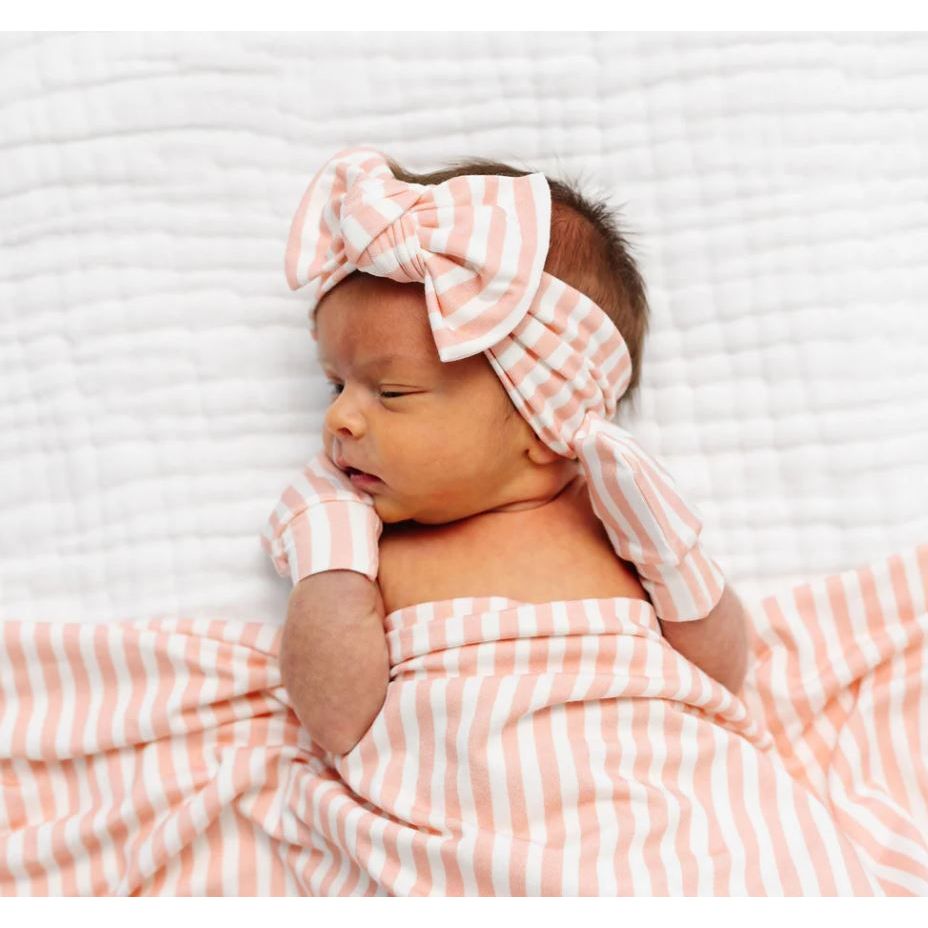 Newborn baby wrapped in a pink and white striped blanket with a matching headband on a white background