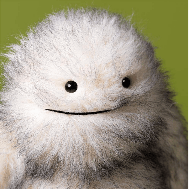 Plush toy with a round face and black eyes on a green background
