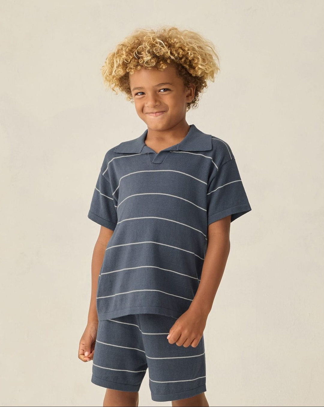 Child wearing a navy striped polo shirt and shorts on a plain background